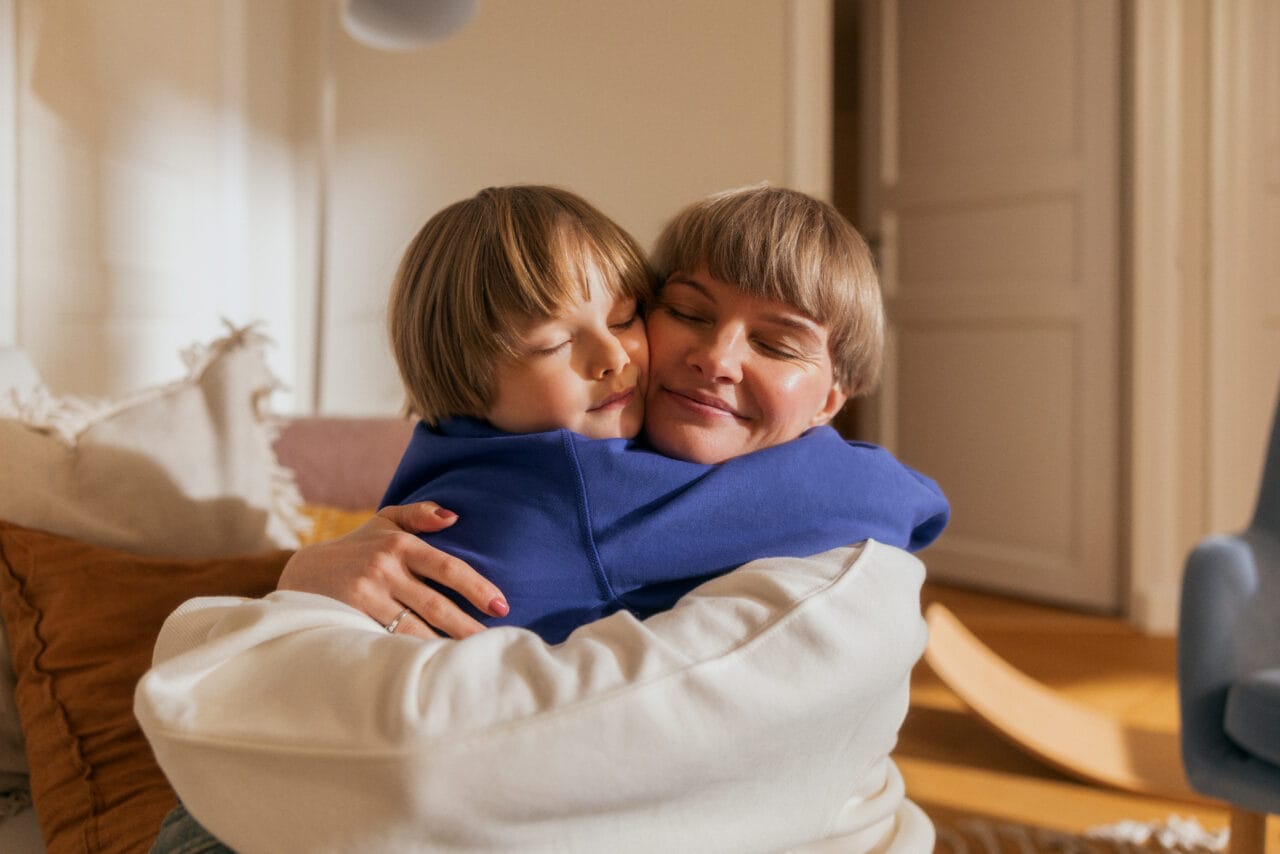 Kuvassa nainen ja lapsi halaavat asunnossa.