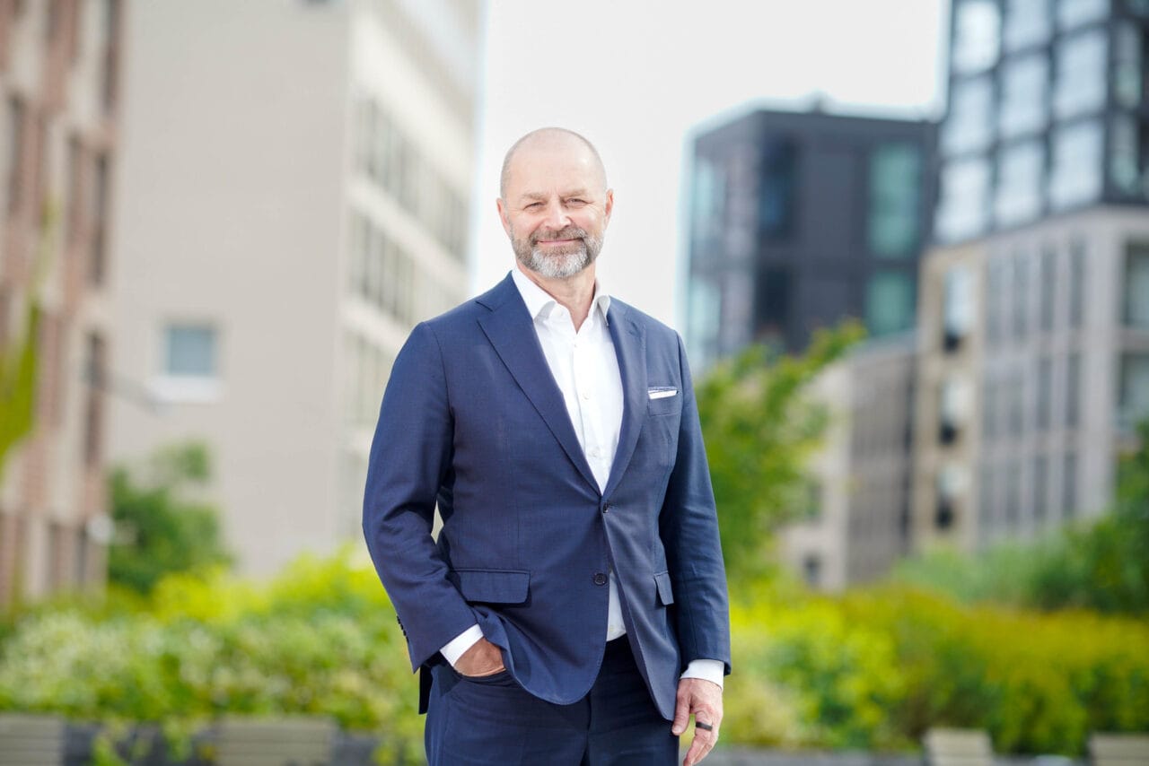 Hymyilevä mies seisomassa pihalla. Taustalla kerrostaloja.