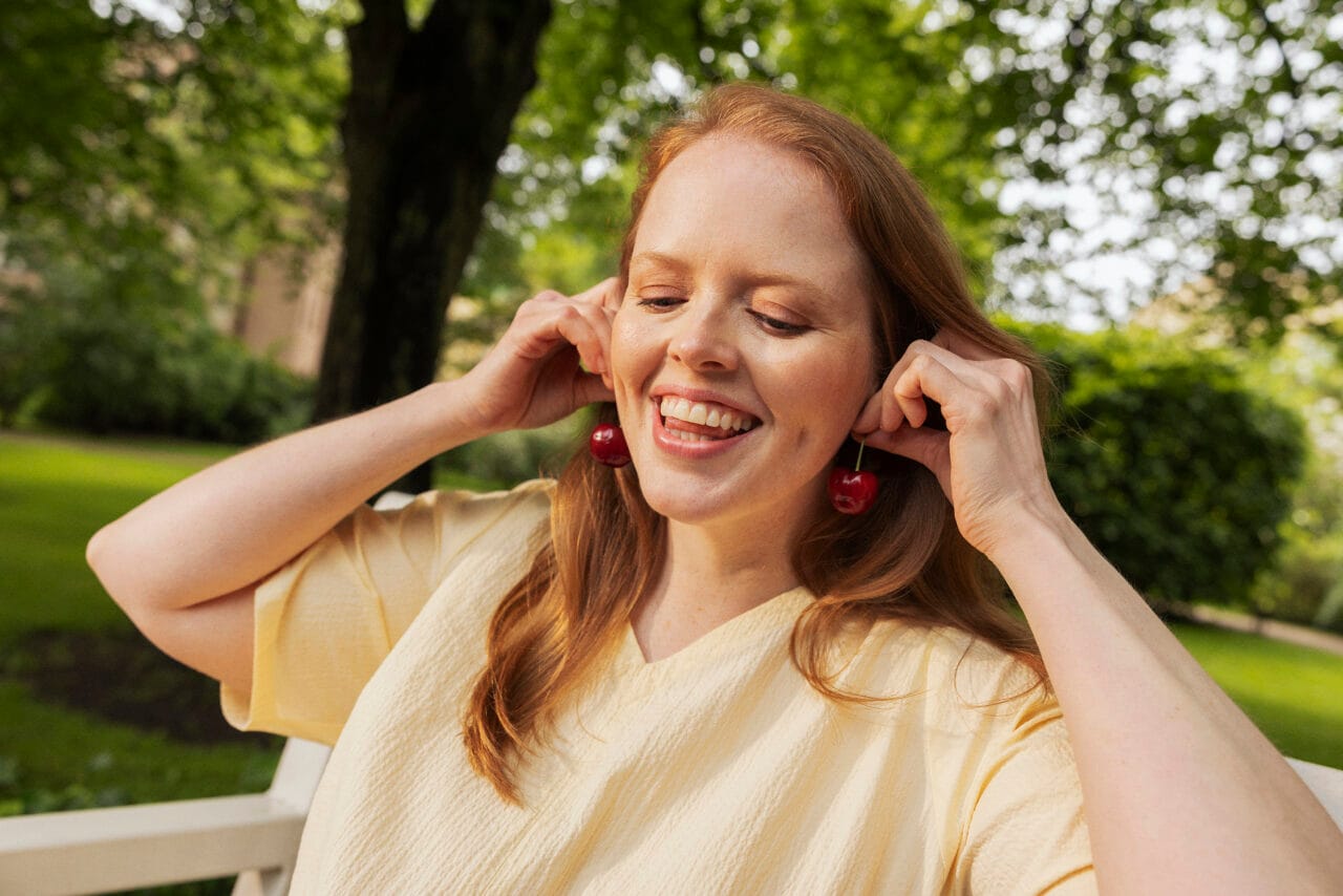 A young woman smiles and holds cherries as earrings.